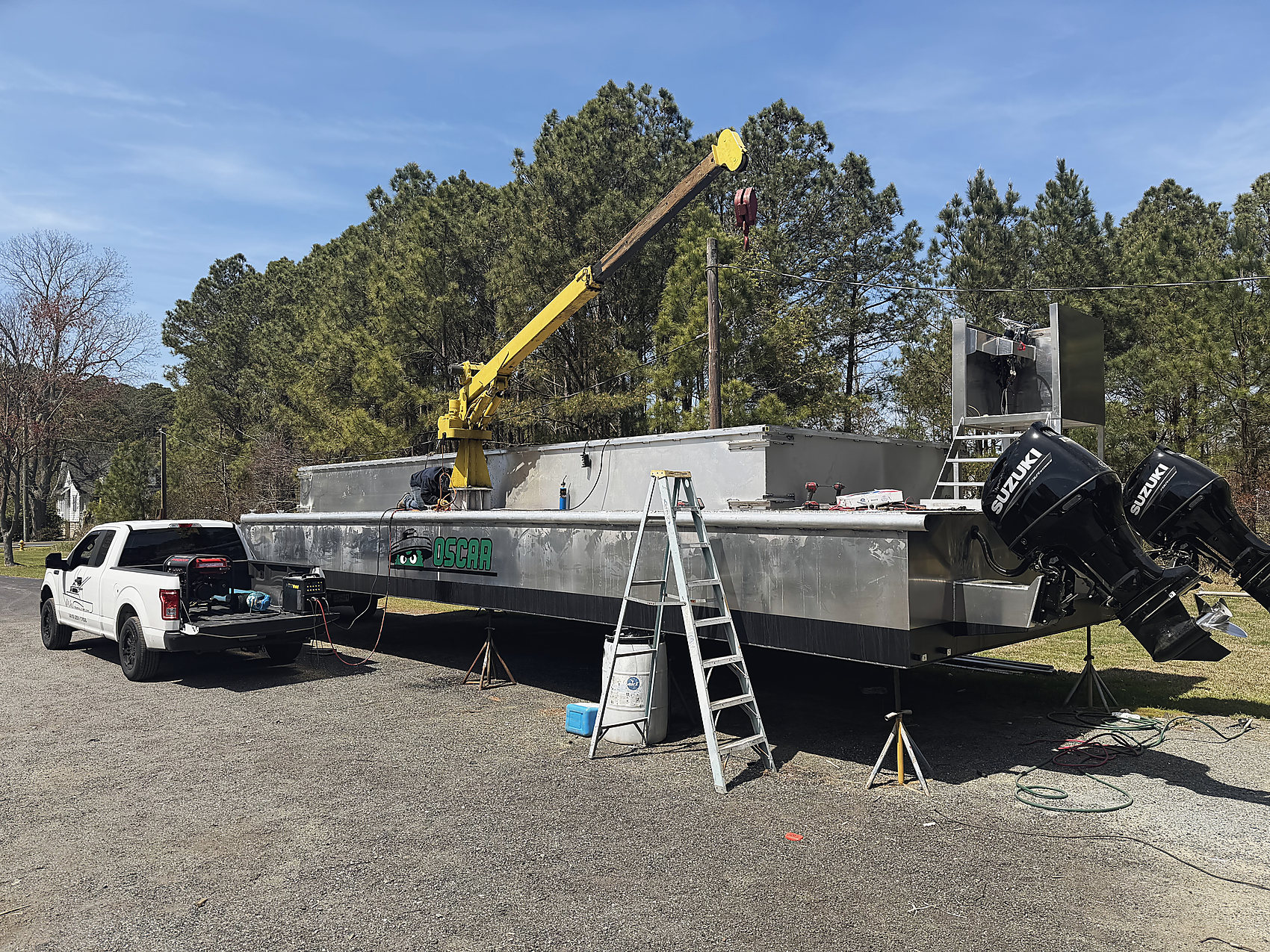 OSCAR, an aluminum boat on the stands, the yellow crane on deck and twin Suzuki outboards on the stern